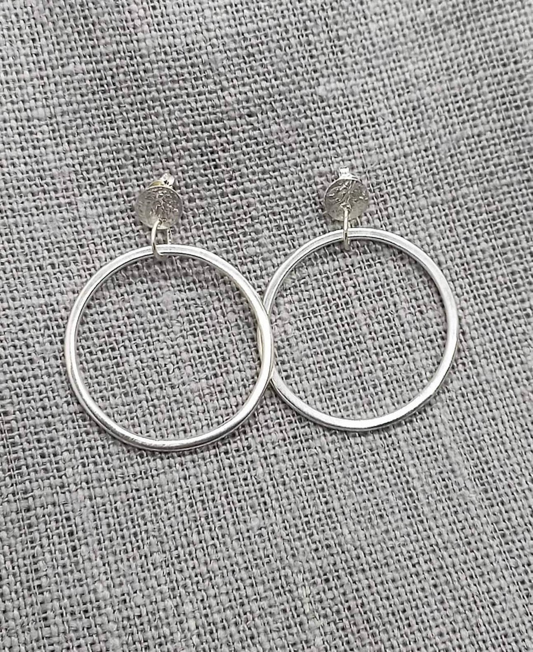 A pair of Amy Iddles Jeweller&#39;s Ripple Loop Earrings on a grey fabric.