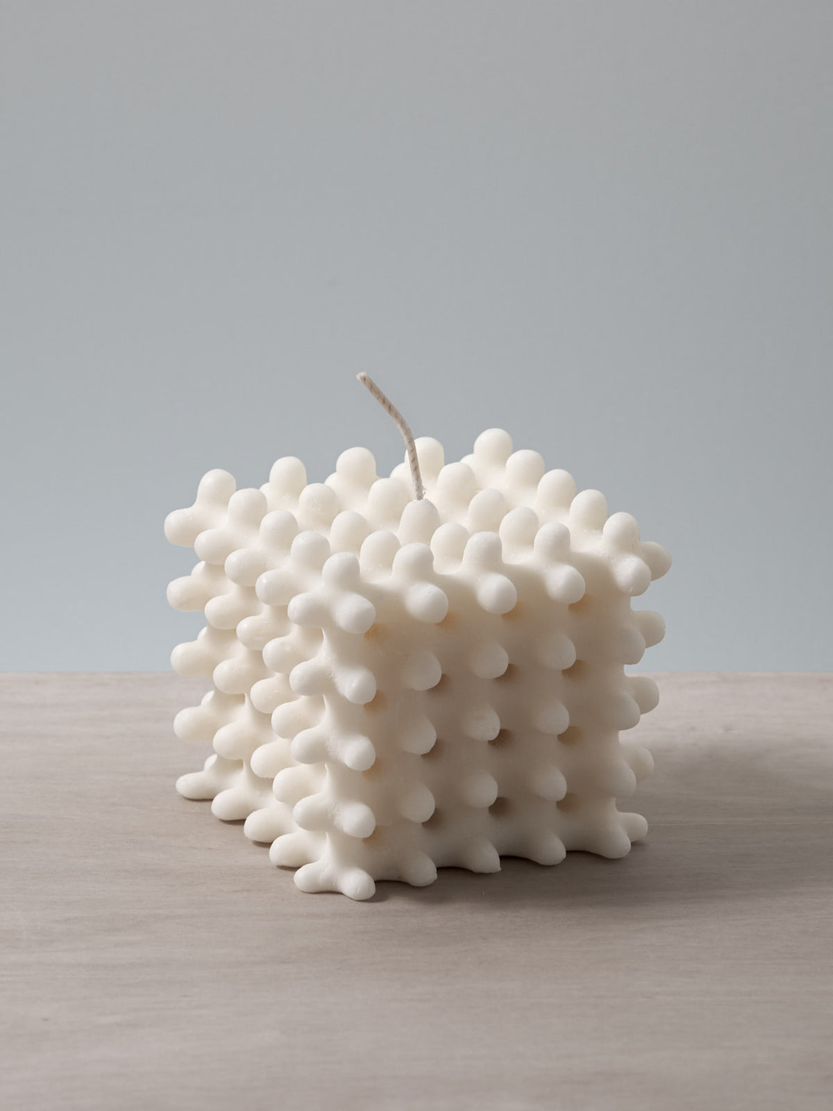 A white Lace Candle shaped like a cube sitting on a table, made by Andrej Urem.