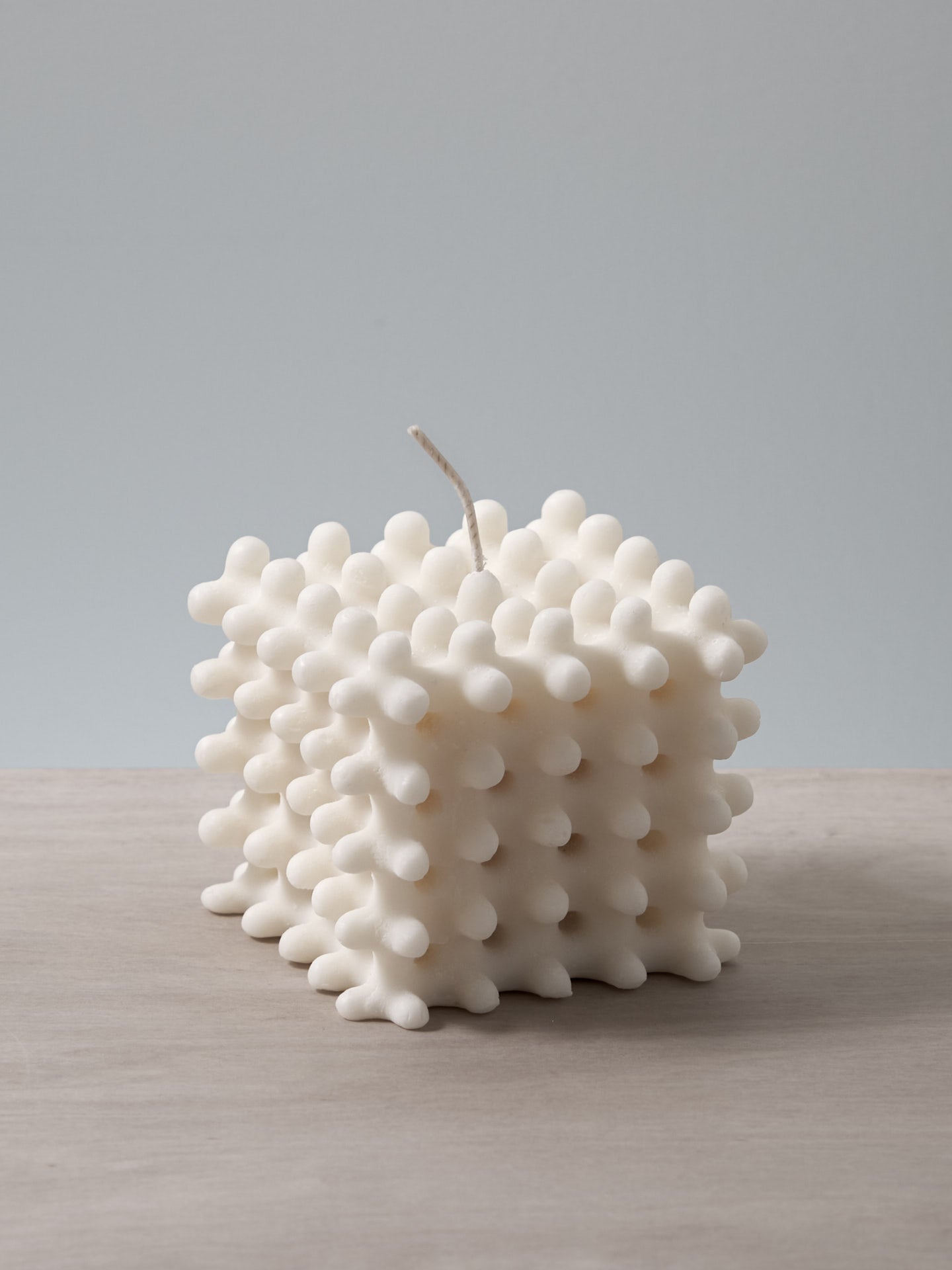 A white Lace Candle shaped like a cube sitting on a table, made by Andrej Urem.