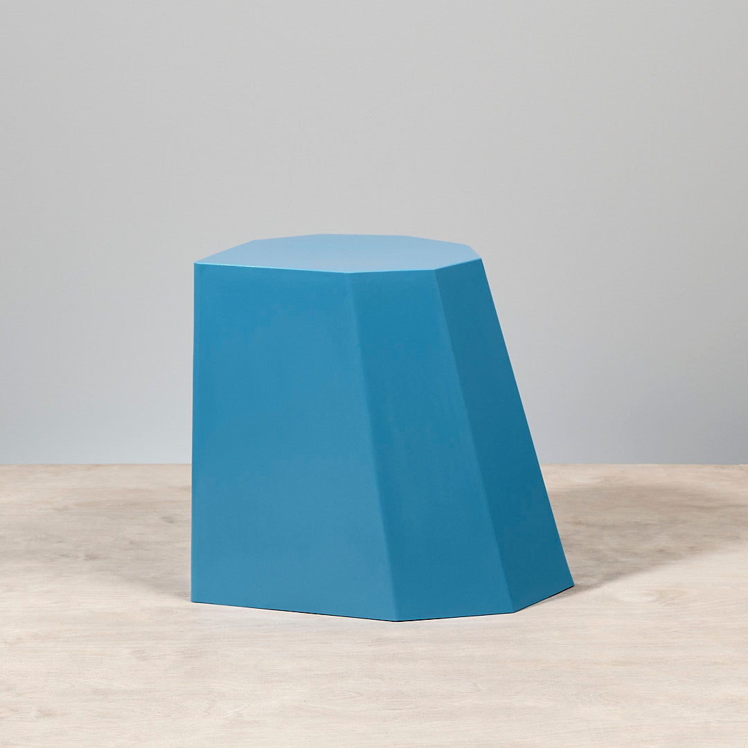 An Arnoldino Stool - Boat Blue sitting on top of a wooden table made by Martino Gamper.