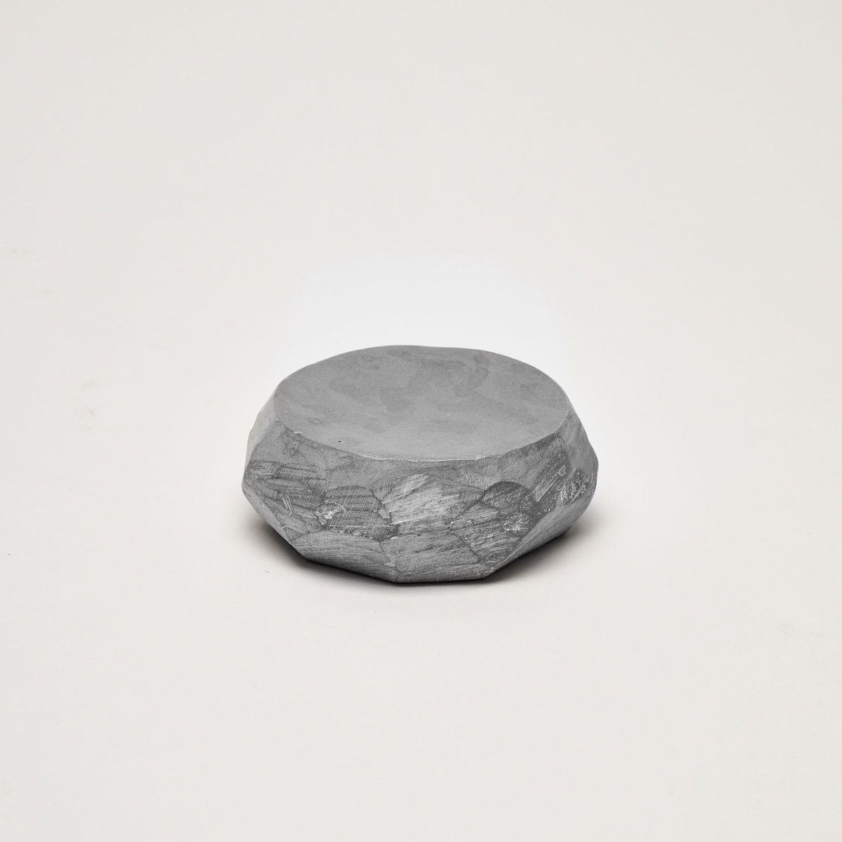 A small round piece of Asili&#39;s Textured Dish Set - Grey sitting on a white surface.