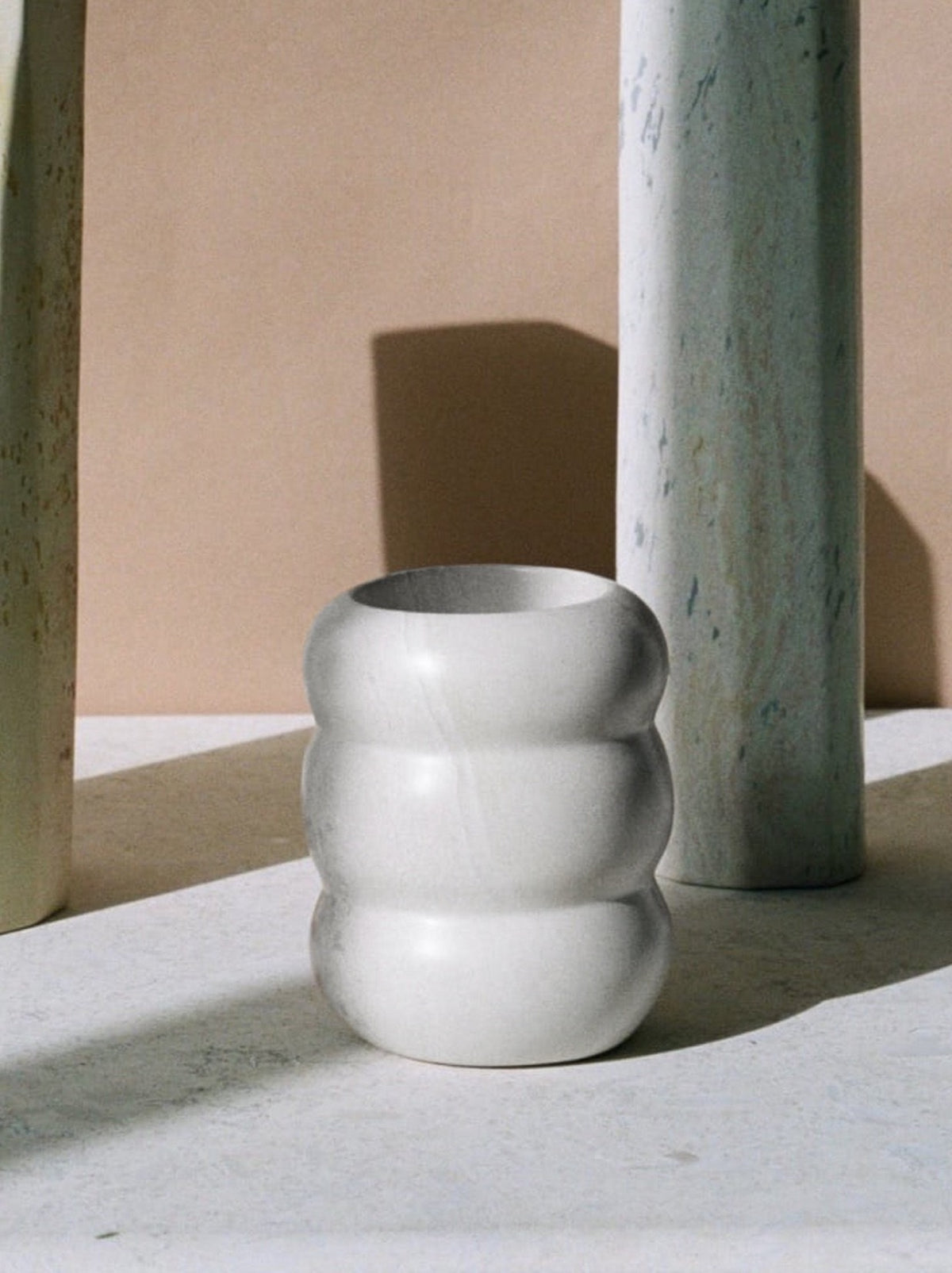 A Roll Vessel - White vase sits on a table next to two other vases.