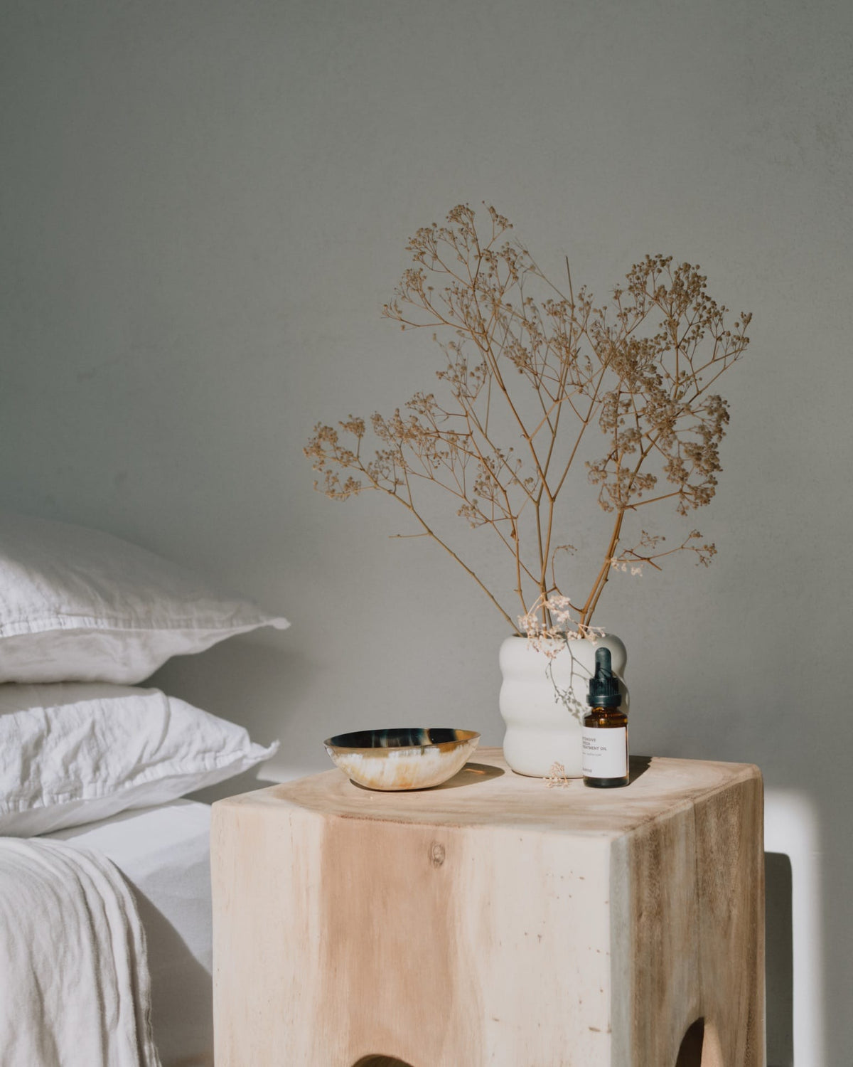 An Asili Roll Vessel – White bedside table with a plant on it.