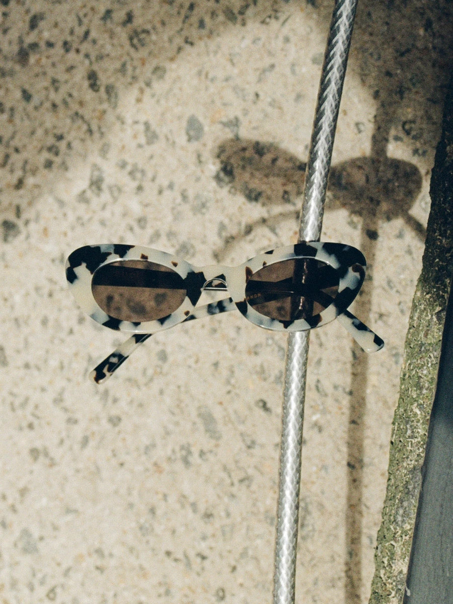 A pair of auór Rosetta Sunglasses – Granite hanging on a pole.