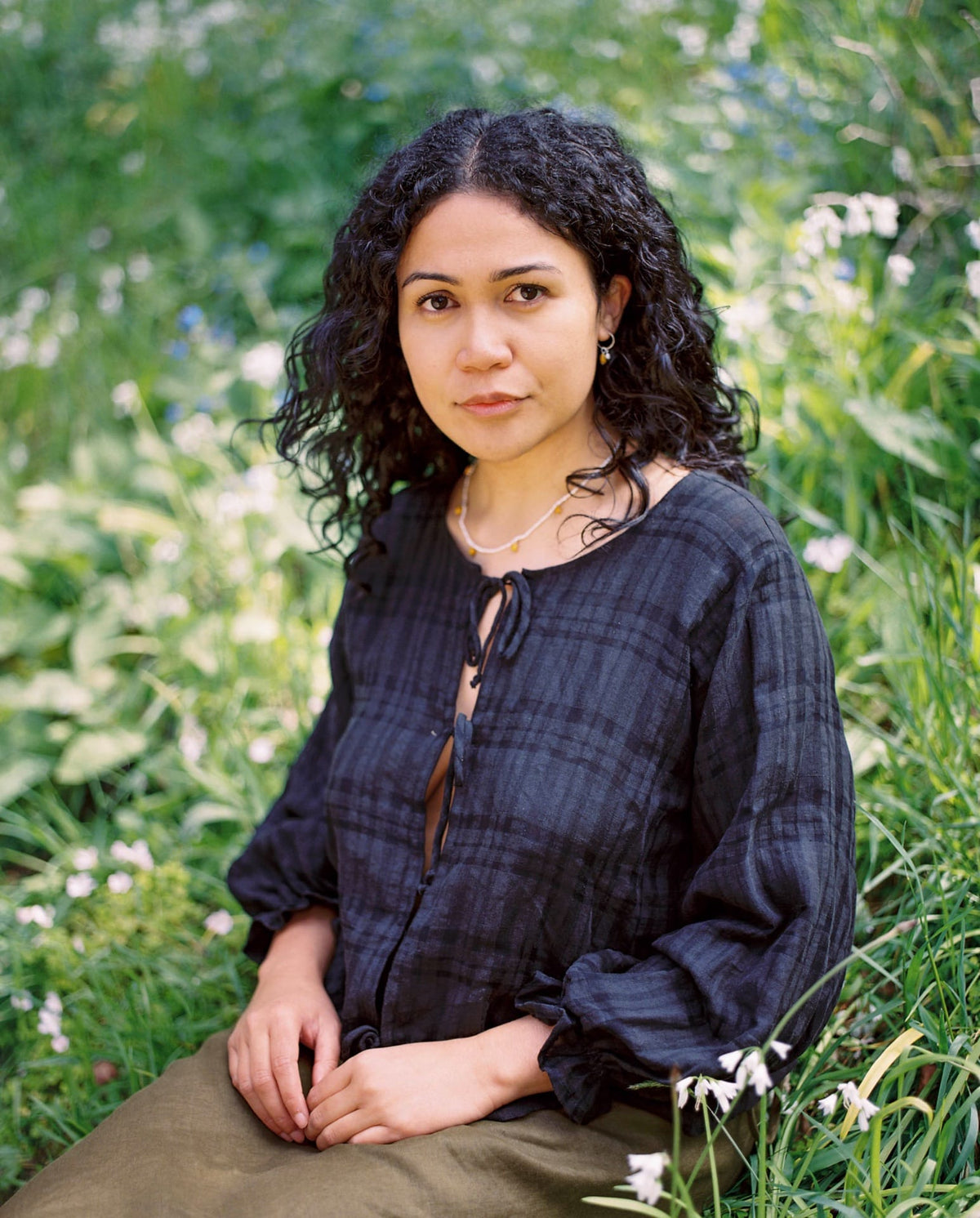 A woman in a black shirt sitting in the grass wearing the Kōwhai Seed Pearl Necklace by Avara Studio.