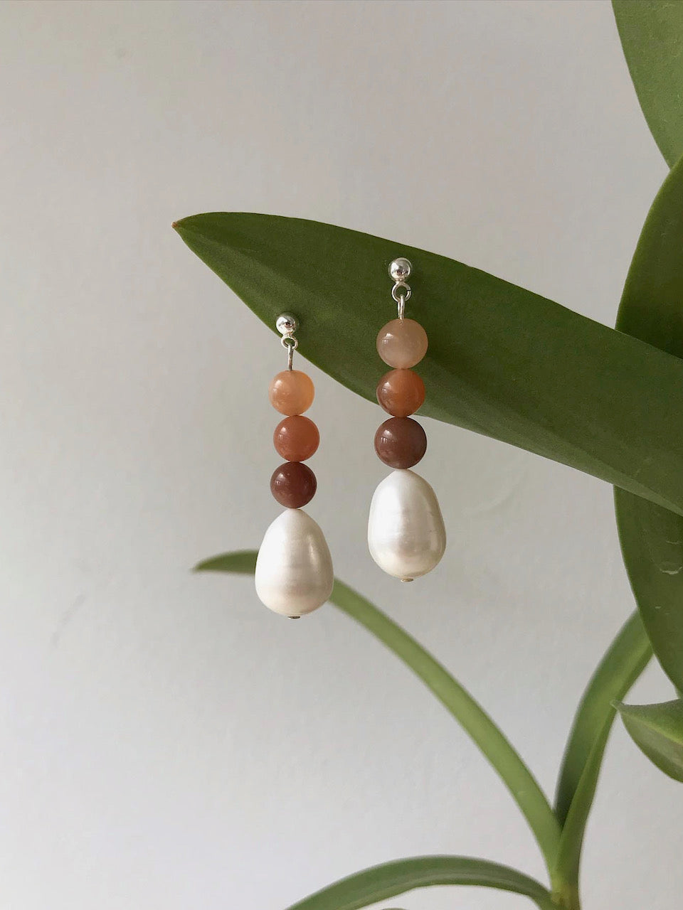 A pair of Horizon Drops earrings from Avara Studio with two pearls hanging from a plant.