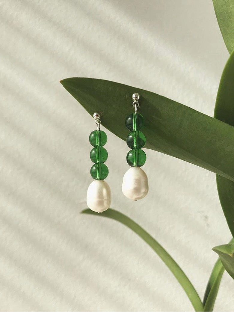 A pair of Jealousy Drops earrings by Avara Studio hanging from a plant.
