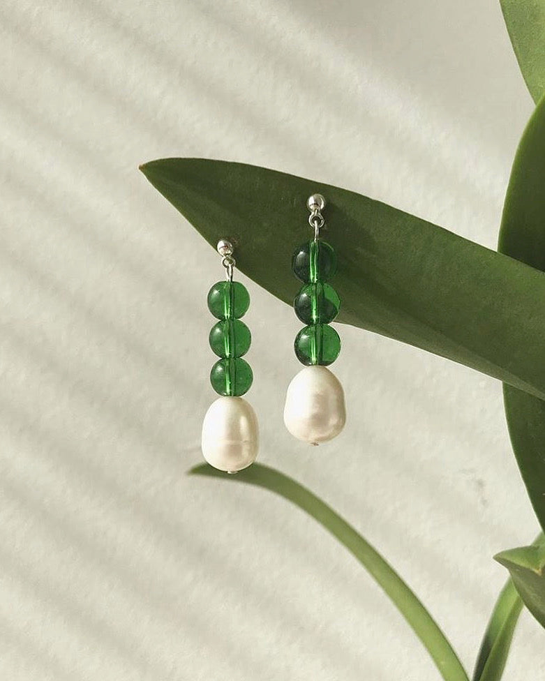 A pair of Jealousy Drops earrings by Avara Studio hanging from a plant.