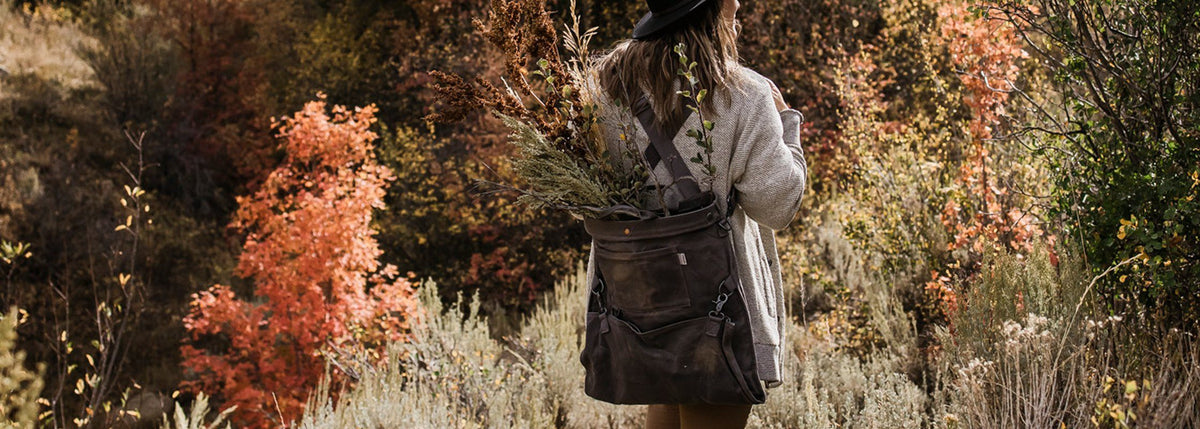 A woman walking through a field with a Barebones Gathering Bag – Grey backpack.