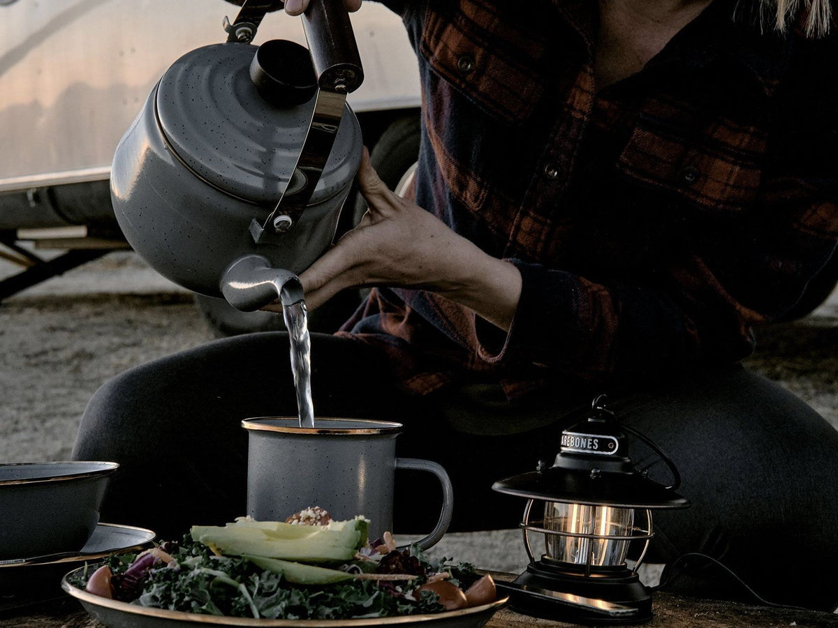 A woman is pouring water into a Barebones Enamel Teapot – Slate Grey in front of a camper.