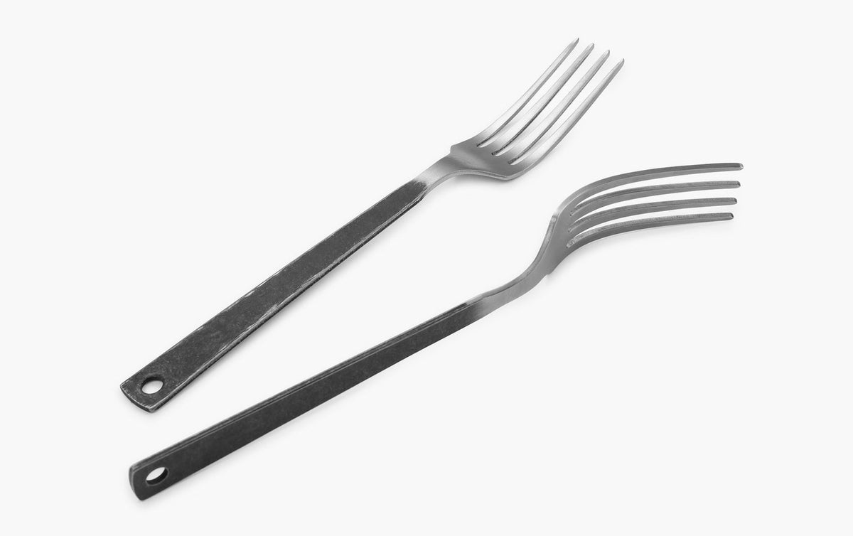 Two Barebones stainless steel forks, part of the Flatware Cutlery set, with long handles and four tines each, arranged parallel on a white background, exude minimalist elegance.