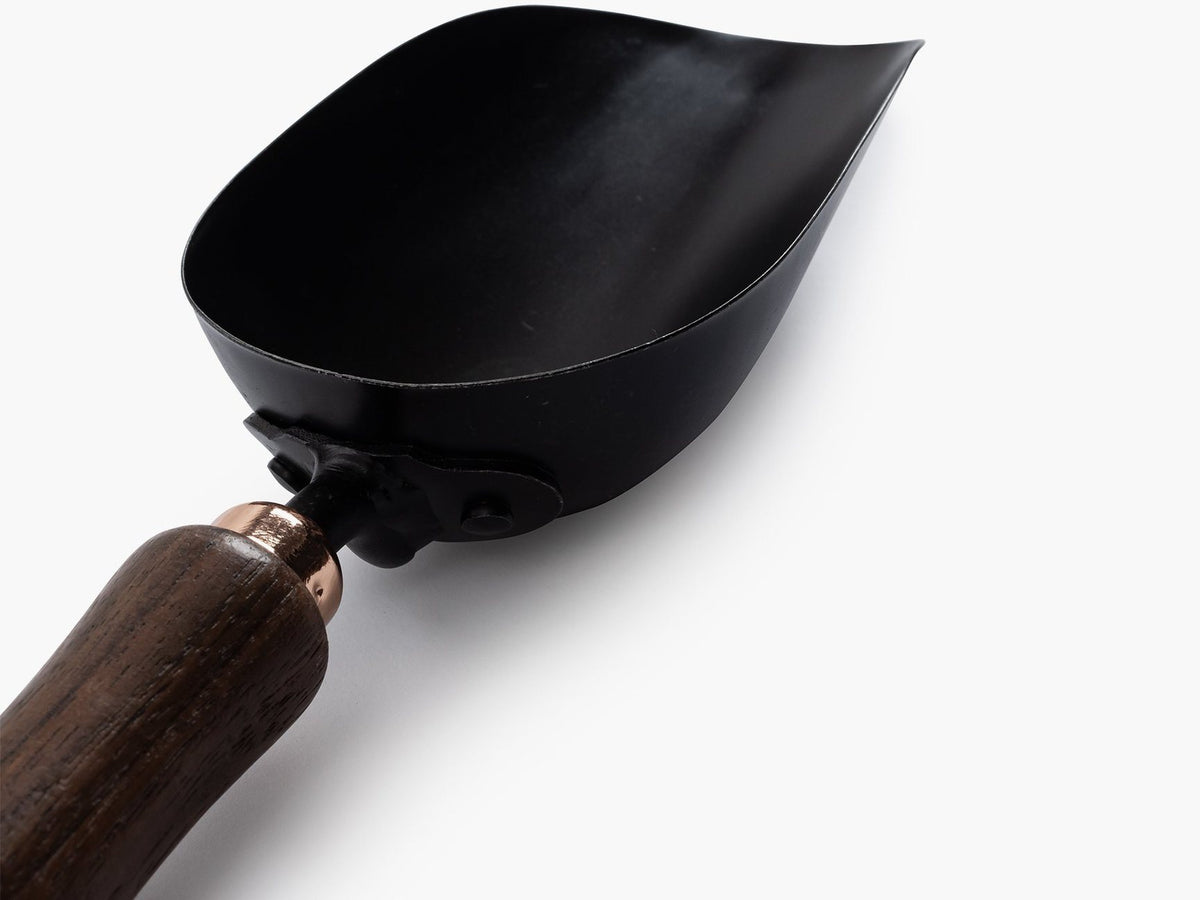 A black Garden Scoop with a wooden handle on a white surface by Barebones.