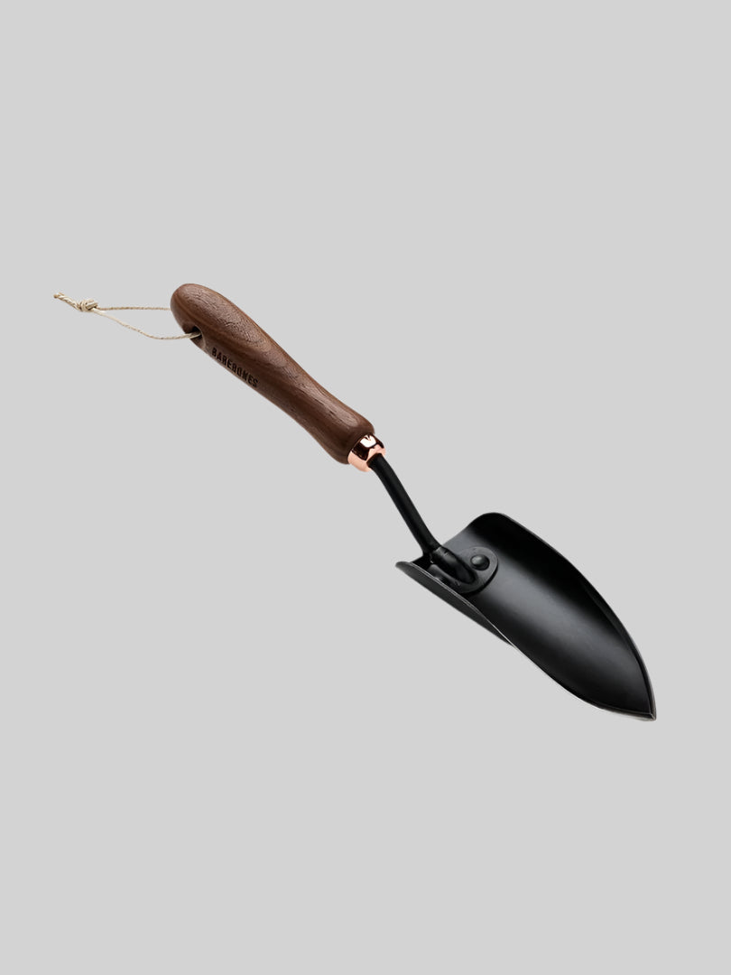 The Walnut Garden Trowel by Barebones showcases an ergonomic design, featuring a wooden handle and a sleek stainless steel blade, elegantly displayed against a plain white background.