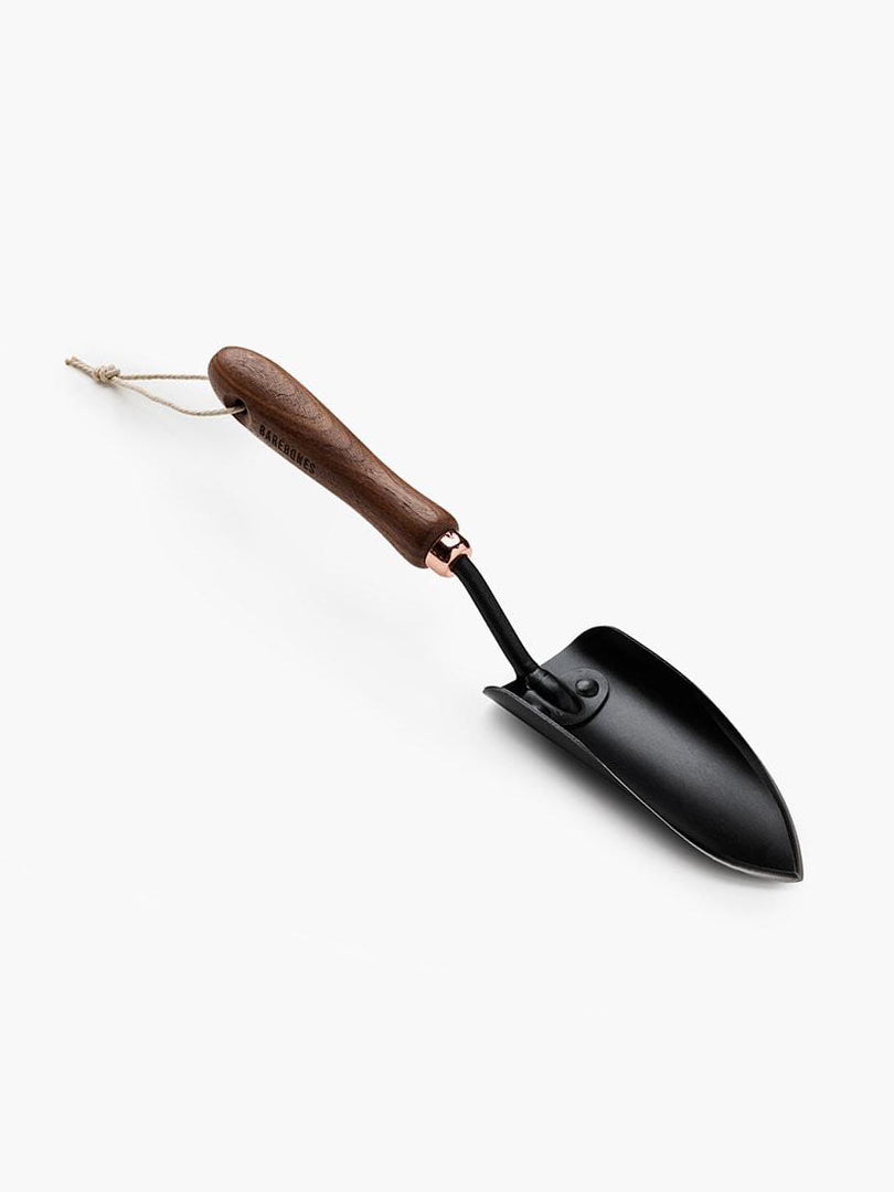 A black Garden Trowel with a wooden handle on a white surface. Brand: Barebones.