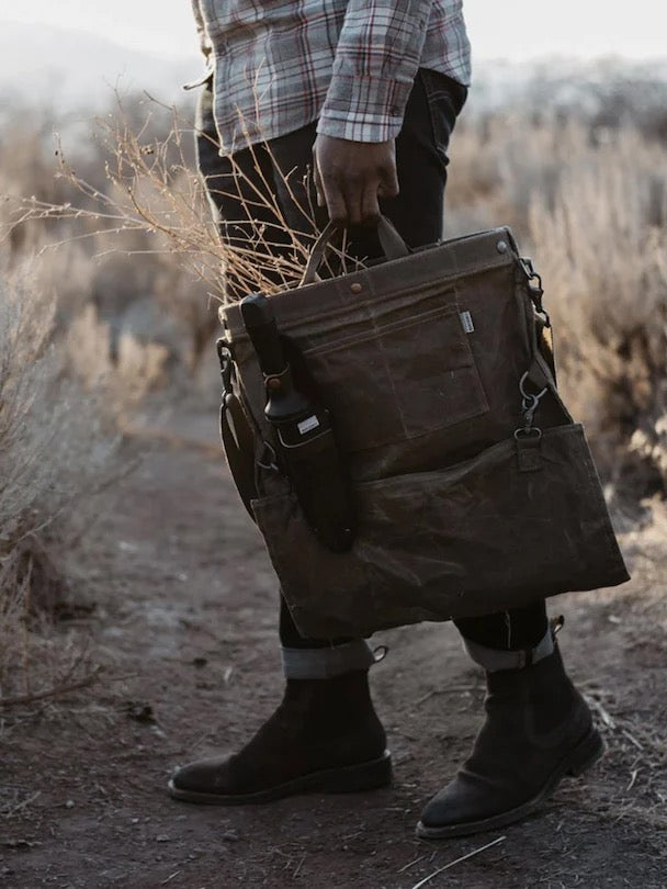 A man carrying a Gathering Bag – Khaki from Barebones in the desert.