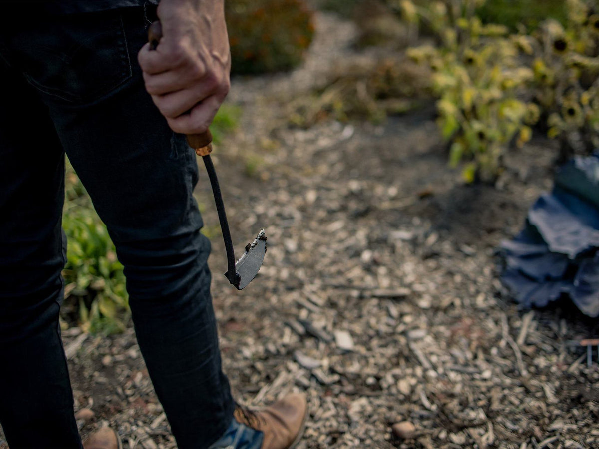 A person holding a Barebones Japanese Weeding Hoe on a dirt path.