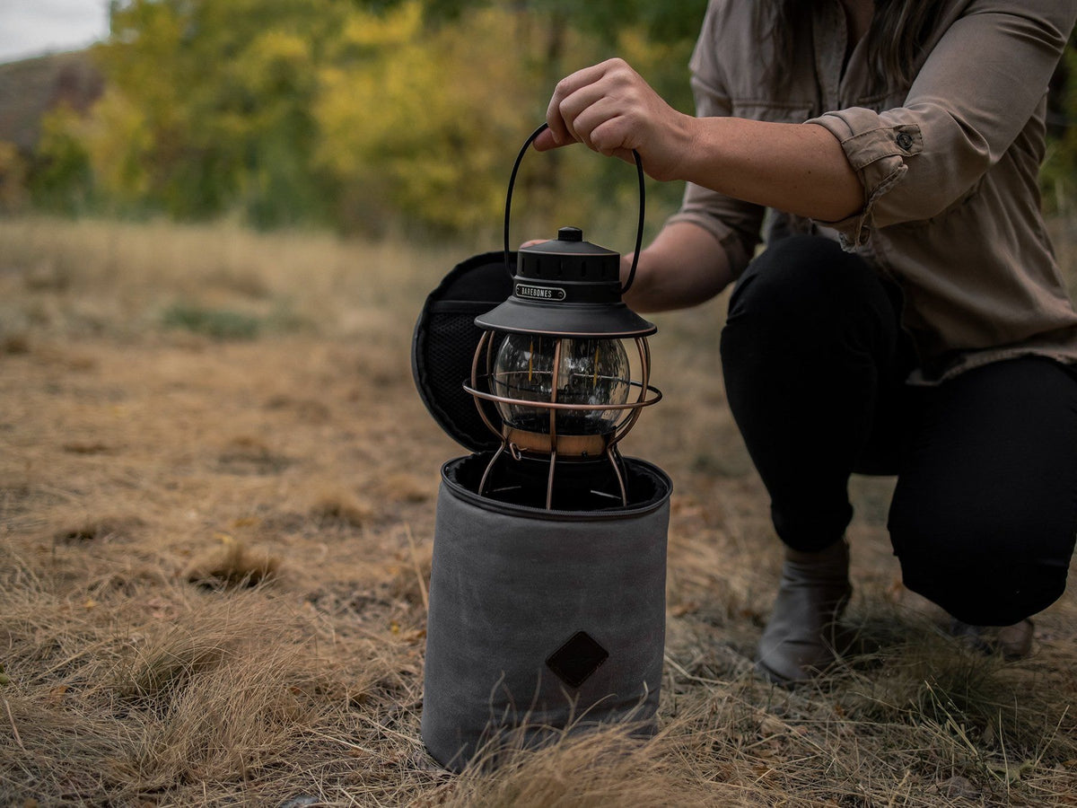 A woman is holding a Barebones Lantern Storage Bag – Waxed Canvas in a field.