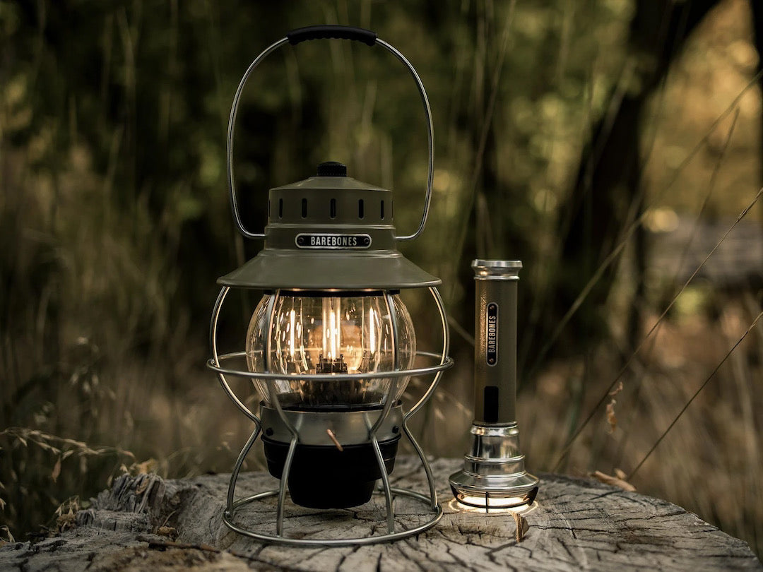 A Barebones Railroad Lantern – Olive Drab sits on top of a log in the woods.