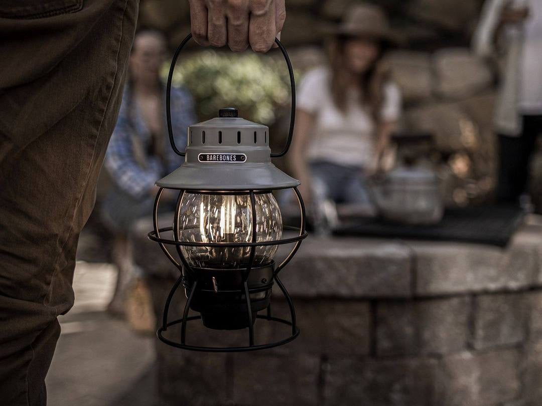A person holding a Barebones Railroad Lantern – Slate Grey in front of a fire pit.
