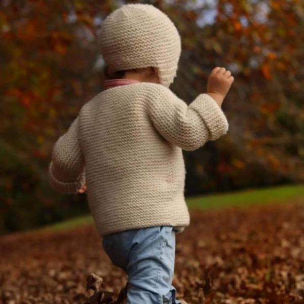 A little boy walking through the leaves in a Weebits Hand Knitted Chunky Knit Hat - Natural.