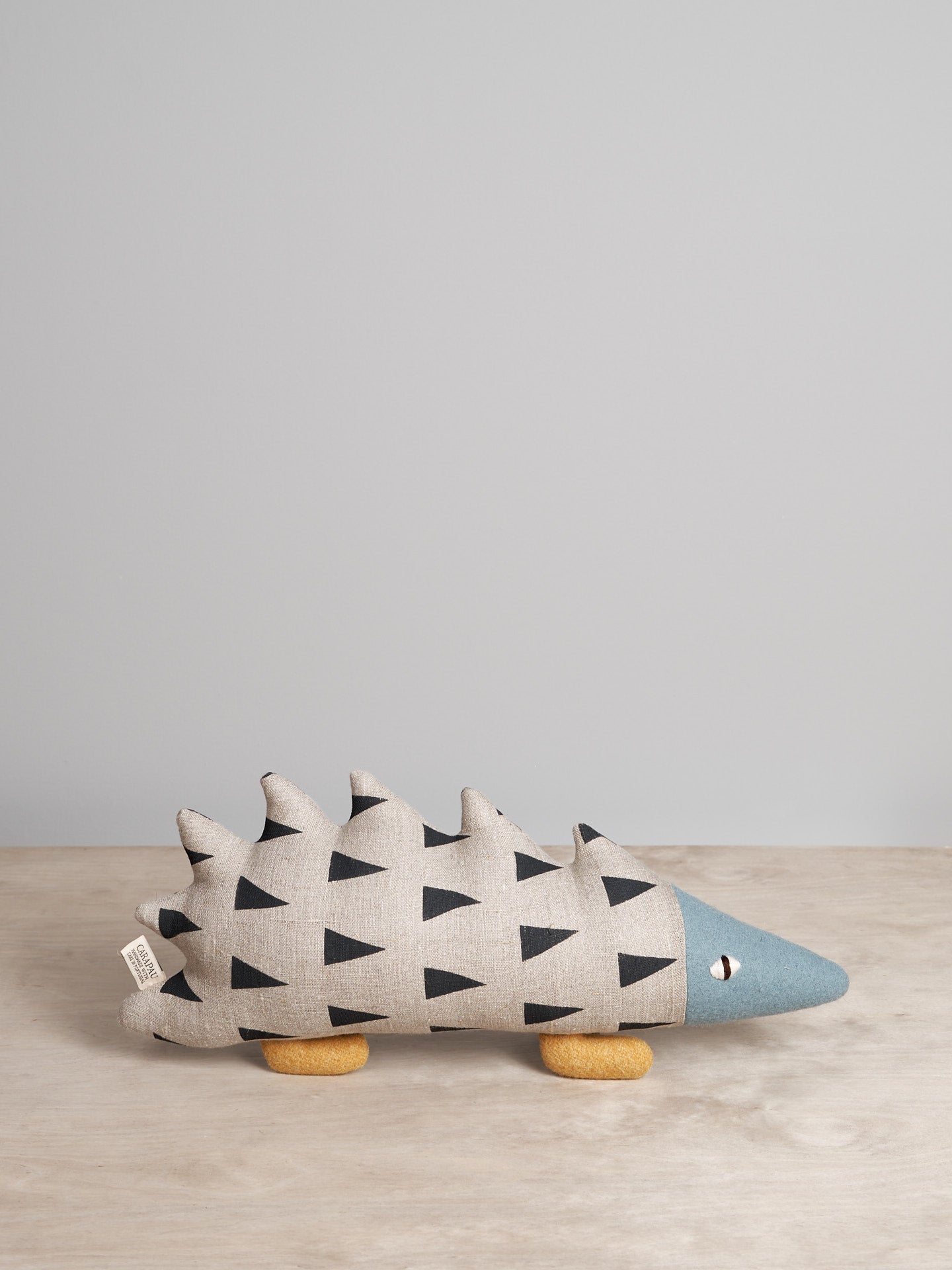 A JIN, the Amur Hedgehog toy sitting on a wooden table, made by Carapau.
