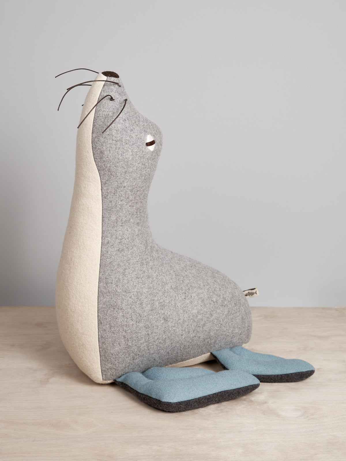 A grey and blue KALI, the Antarctic Fur Seal stuffed animal sitting on a table. (Brand: Carapau)