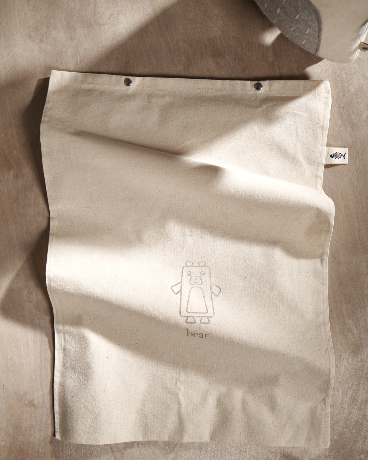 A NASH bag with a bear on it next to a wooden table. (Brand: Carapau)