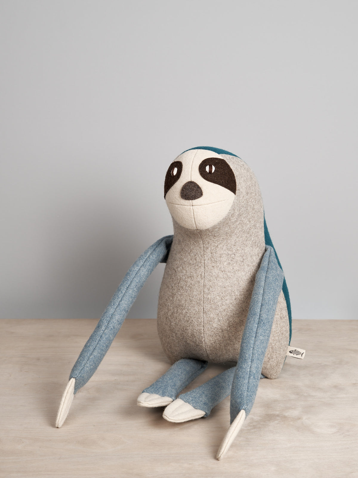 A NED, the Brown-Throated Sloth stuffed animal sitting on a wooden table from Carapau.
