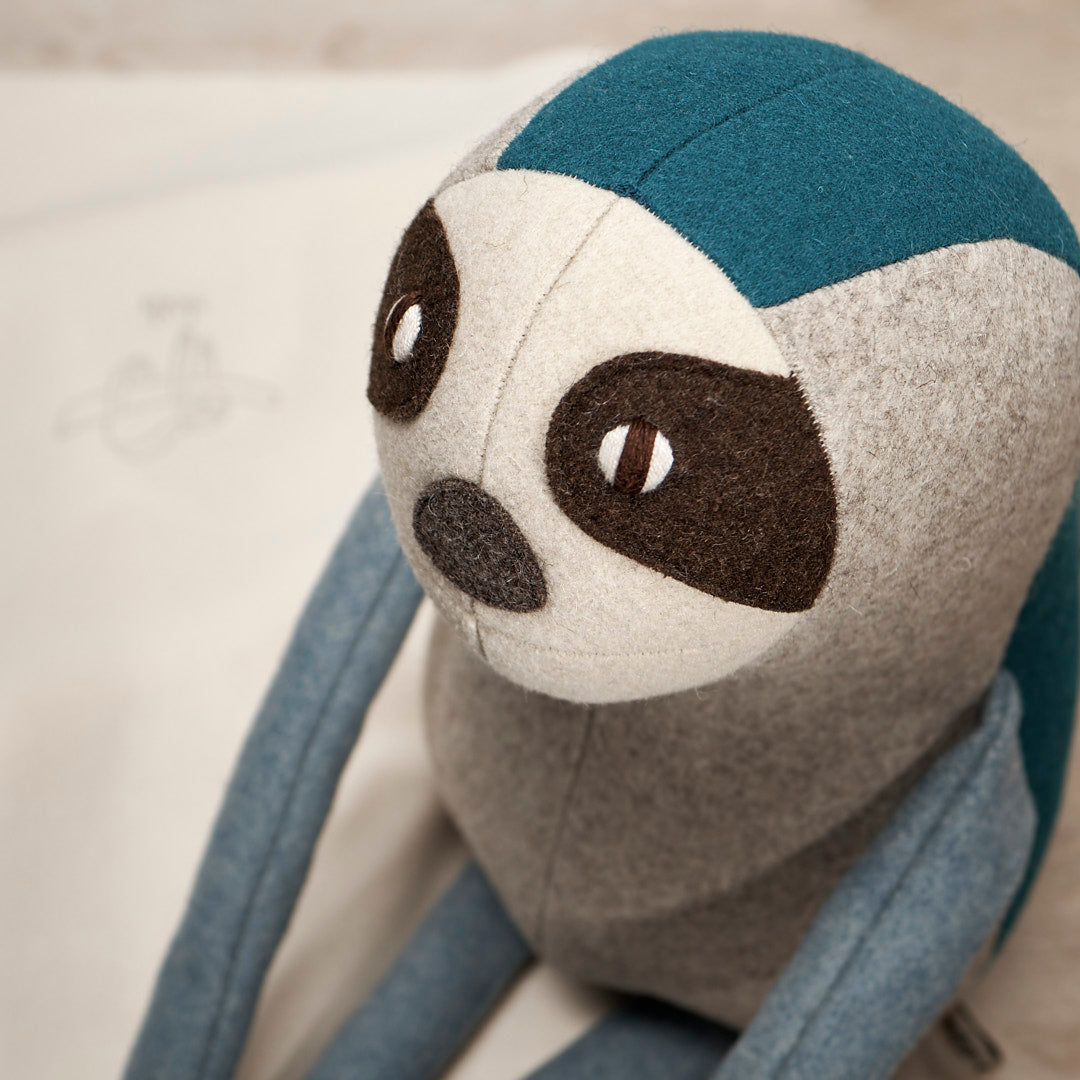 A NED, the Brown-Throated Sloth stuffed animal is sitting on top of a piece of paper. (Brand: Carapau)