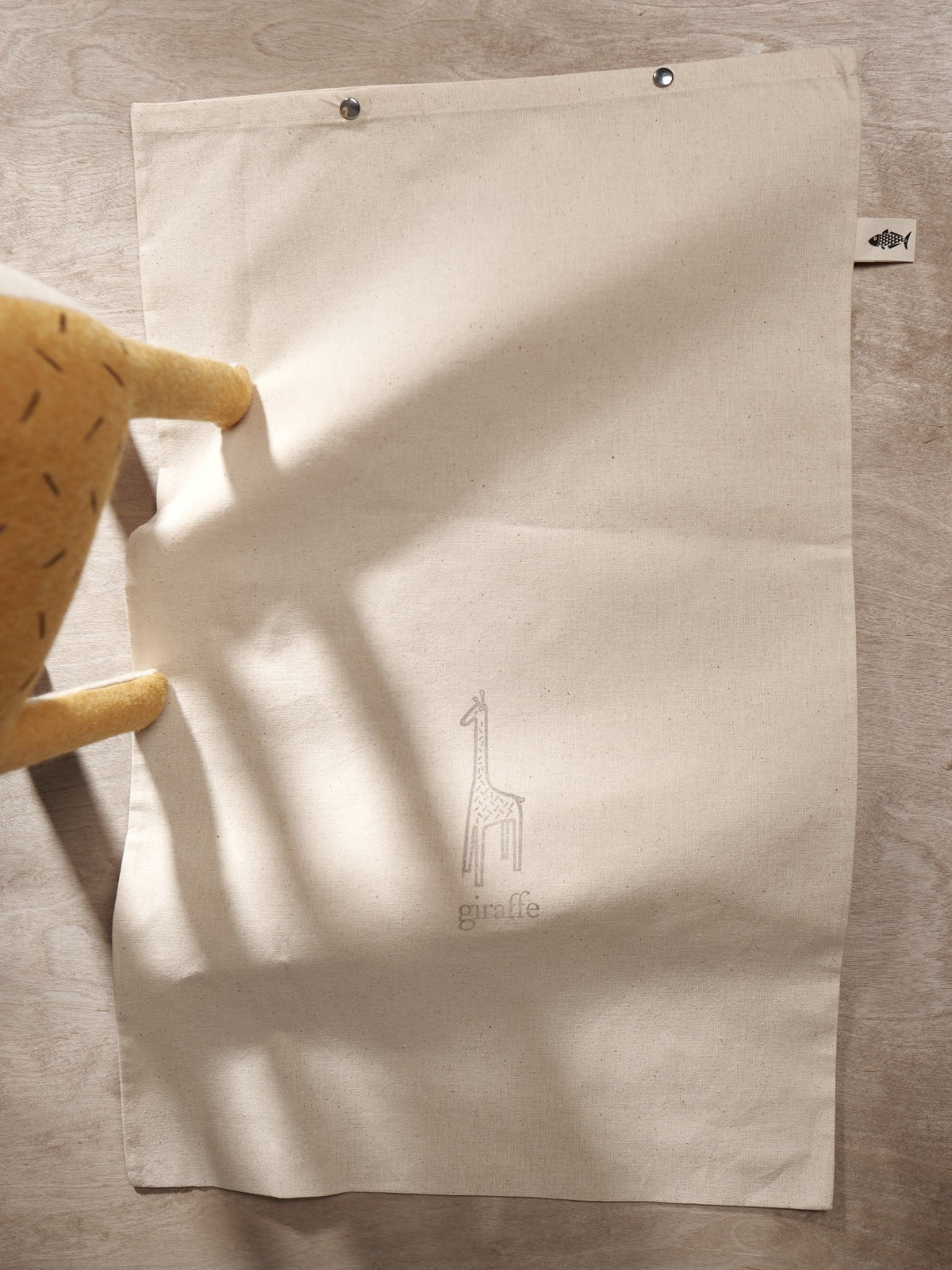 A ZIFFA, the Nubian giraffe stuffed animal is sitting on top of a Carapau towel.