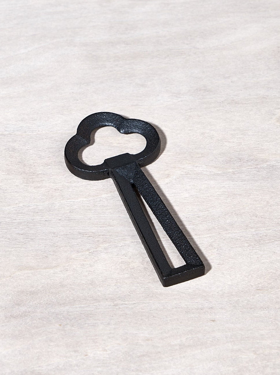 A Clover Bottle Opener – Black key shaped like a cloud on a wooden surface.