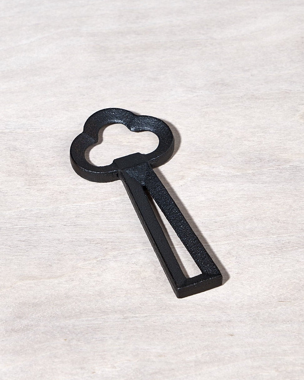 A Clover Bottle Opener – Black key shaped like a cloud on a wooden surface.