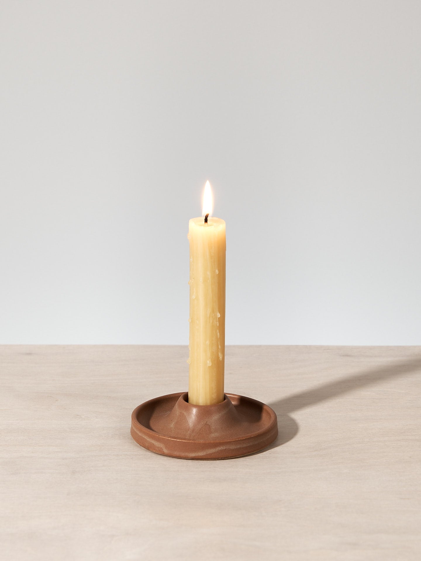 A Deborah Sweeney Candle Holder - Ochre sitting on a wooden table.
