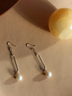 A pair of Baroque Pearl Earrings by EMBR Jewellery on a table next to a yellow ball.