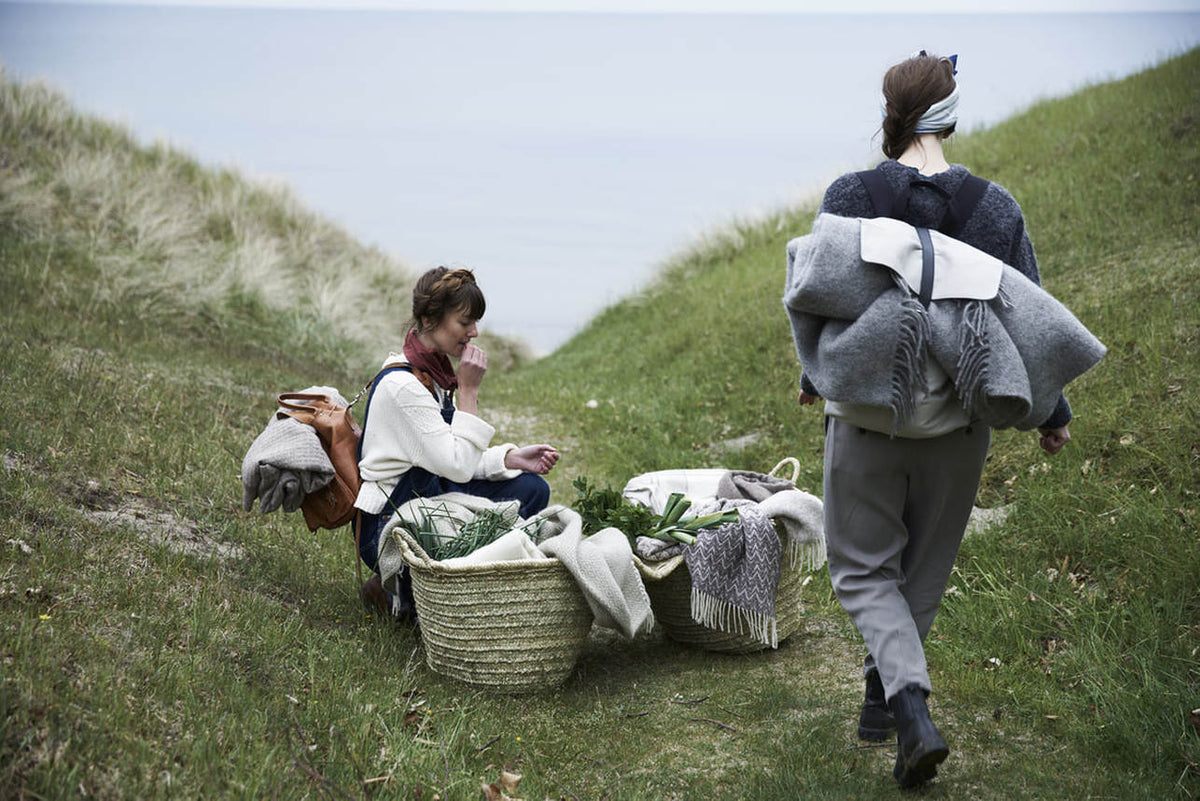 Two women walking down a hill with baskets of Klippan Earth Blanket – Grey.