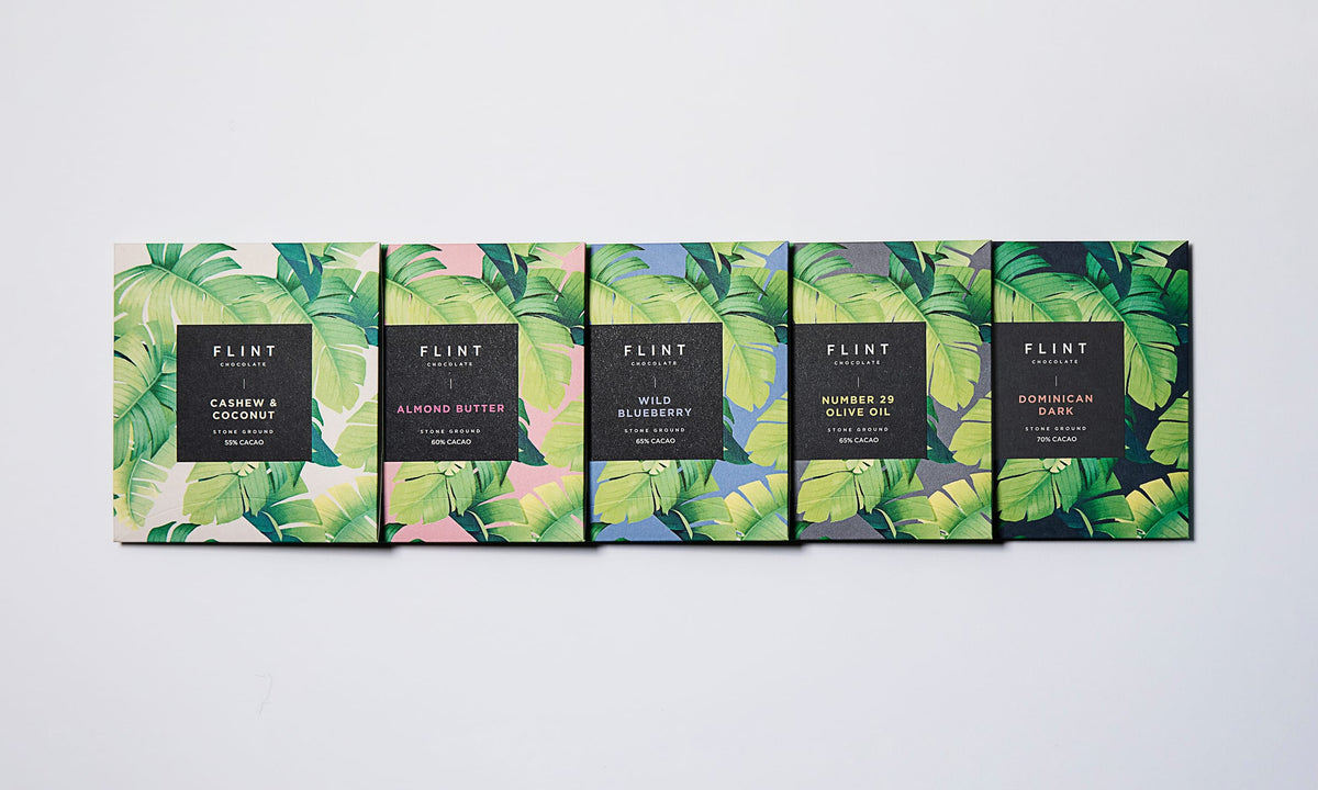 Five Almond Butter Chocolate Bars with tropical leaves on a white background. (Brand Name: Flint Chocolate)