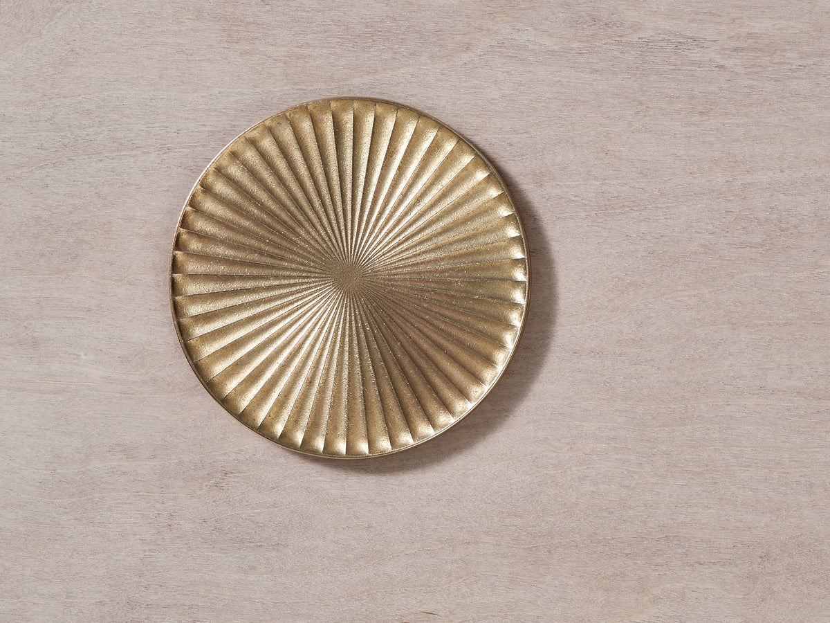 A Futagami Kobo Coaster – Solid Brass plate on a wooden surface.