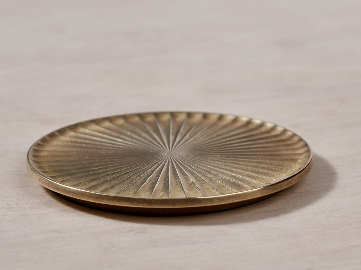 A Kobo Coaster - Solid Brass with a sunburst pattern on it. Brand: Futagami.