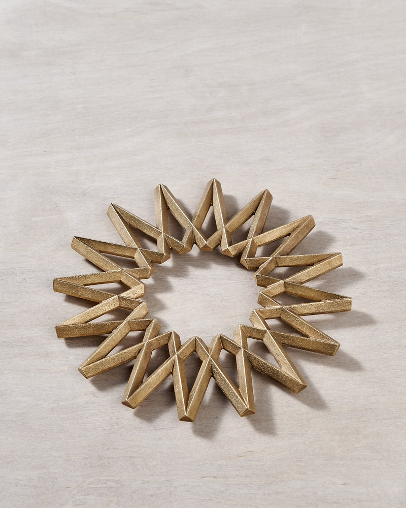 A Galaxy Trivet - Solid Brass bracelet by Futagami on a wooden surface.