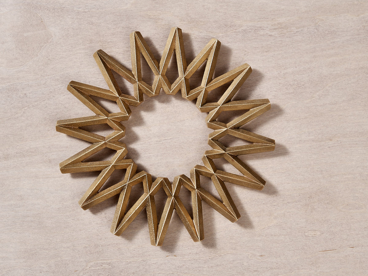 A Galaxy Trivet – Solid Brass star shaped ornament on a wooden surface from Futagami.