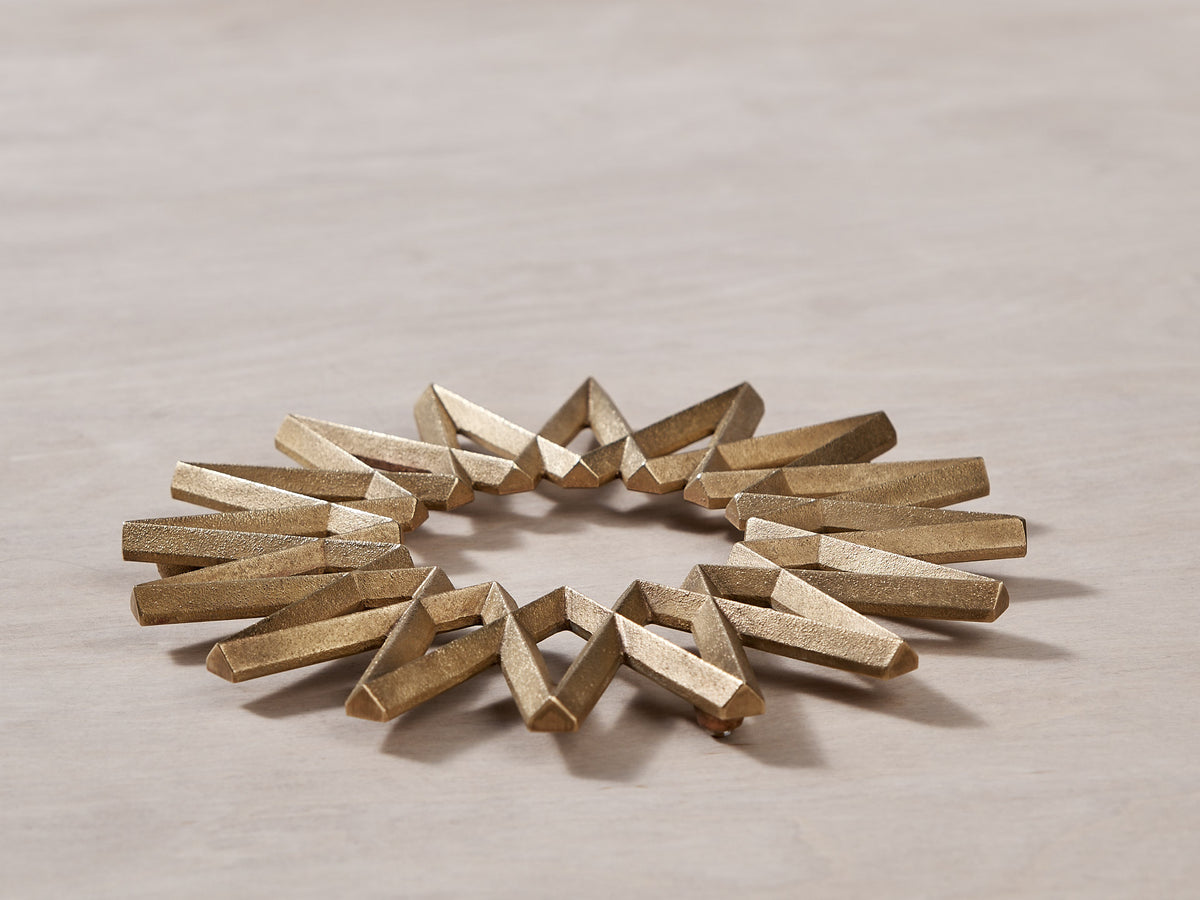 A Galaxy Trivet – Solid Brass starburst bracelet on a wooden surface by Futagami.