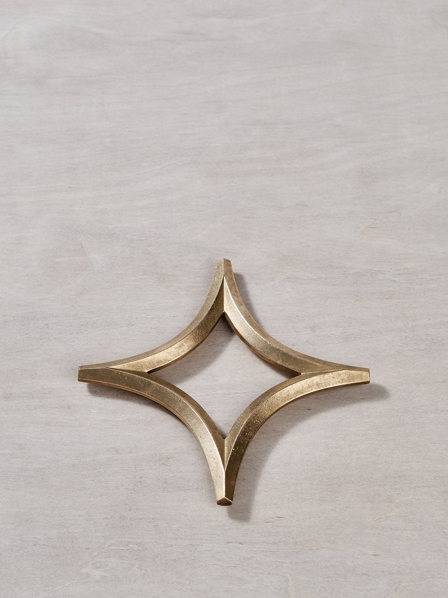 A Star Trivet – Solid Brass by Futagami on a wooden surface.