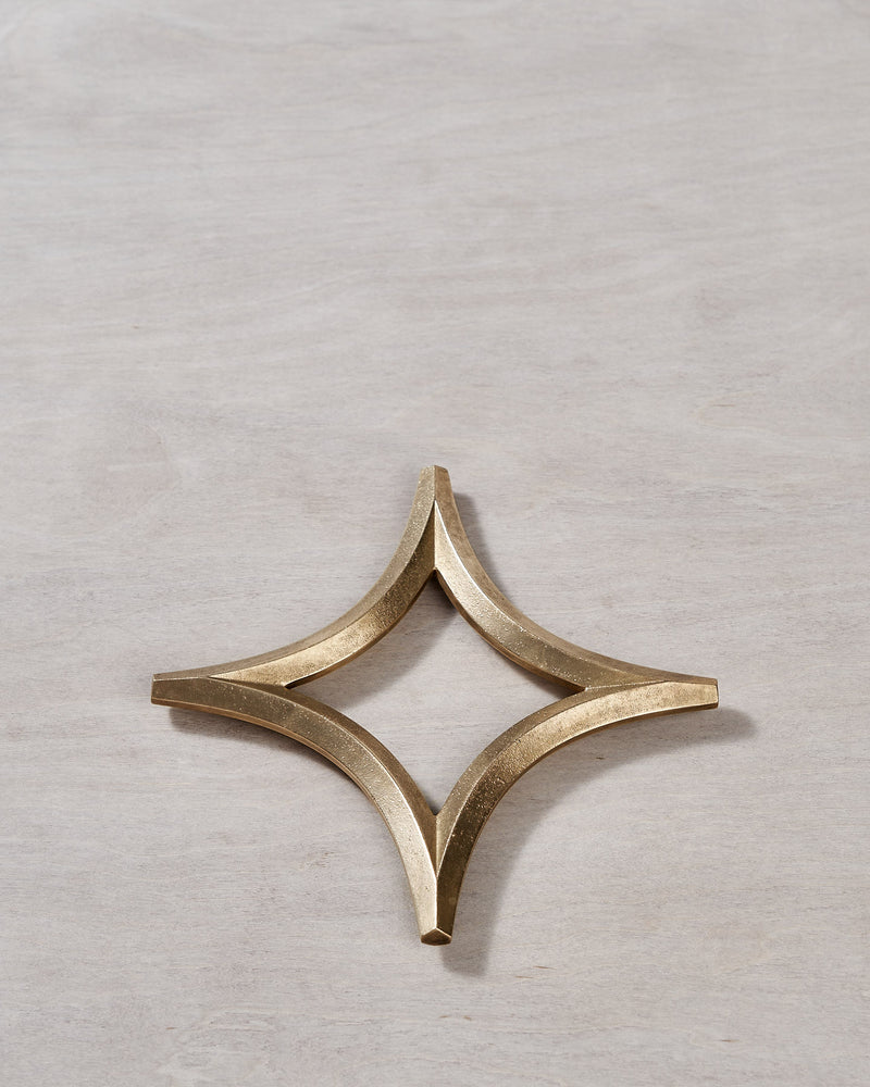 A Star Trivet – Solid Brass by Futagami on a wooden surface.