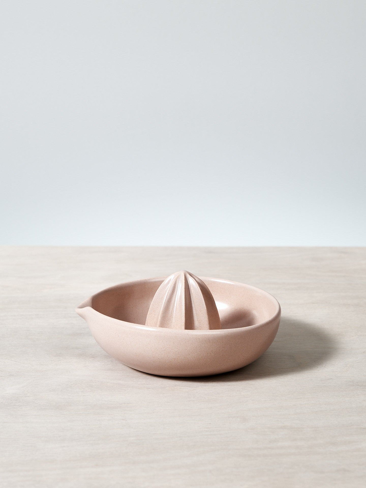A pink Citrus Juicer – Dusty Pink by Gidon Bing sitting on top of a wooden table.