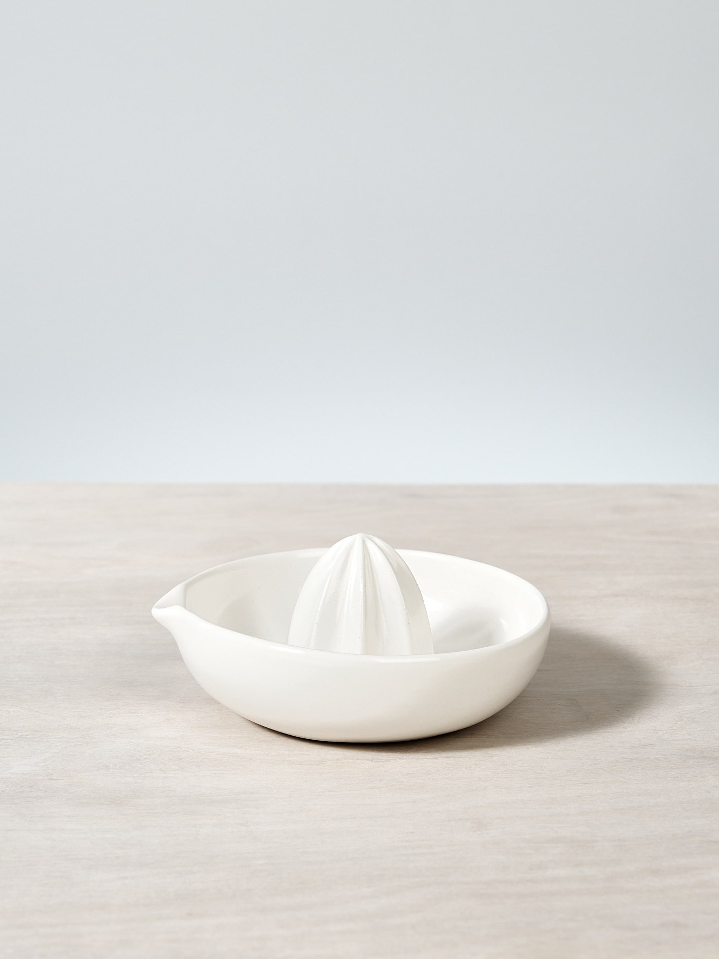 A Citrus Juicer – Satin White by Gidon Bing sitting on top of a wooden table.