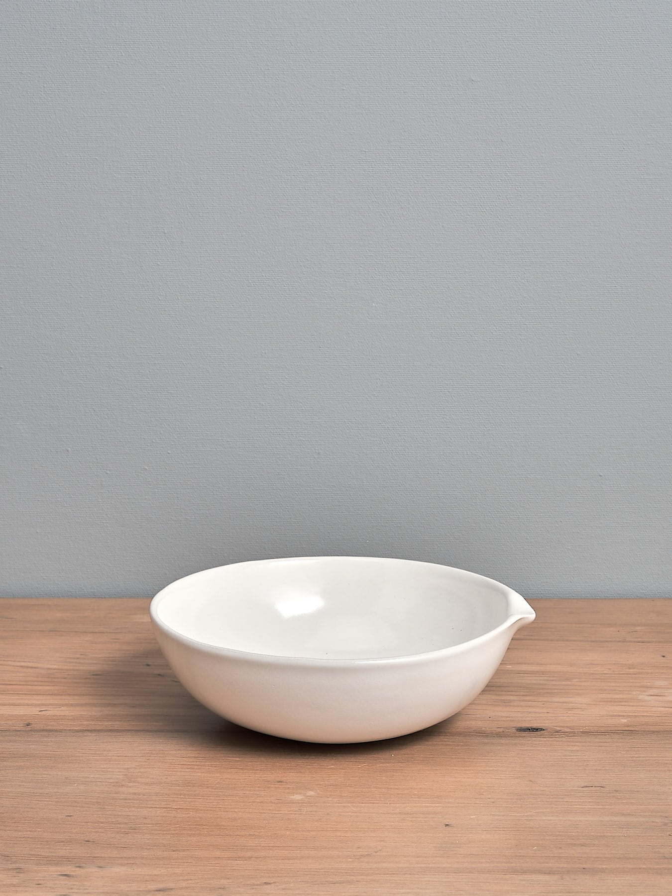 A Medium Lab Bowl - Satin White by Gidon Bing sitting on a wooden table.