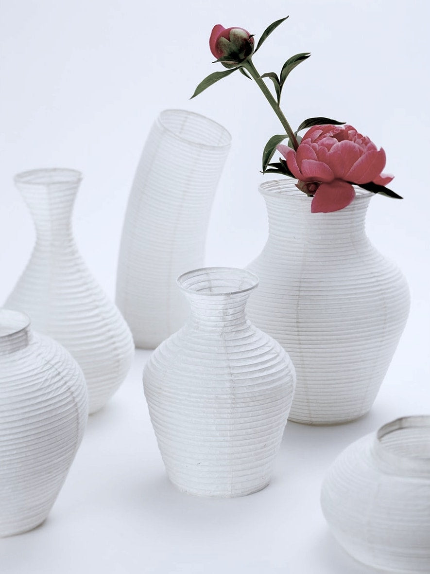 A group of Nobi-tsutsu Paper Vases – №1 by Hayashi Kougei with a pink flower in them.