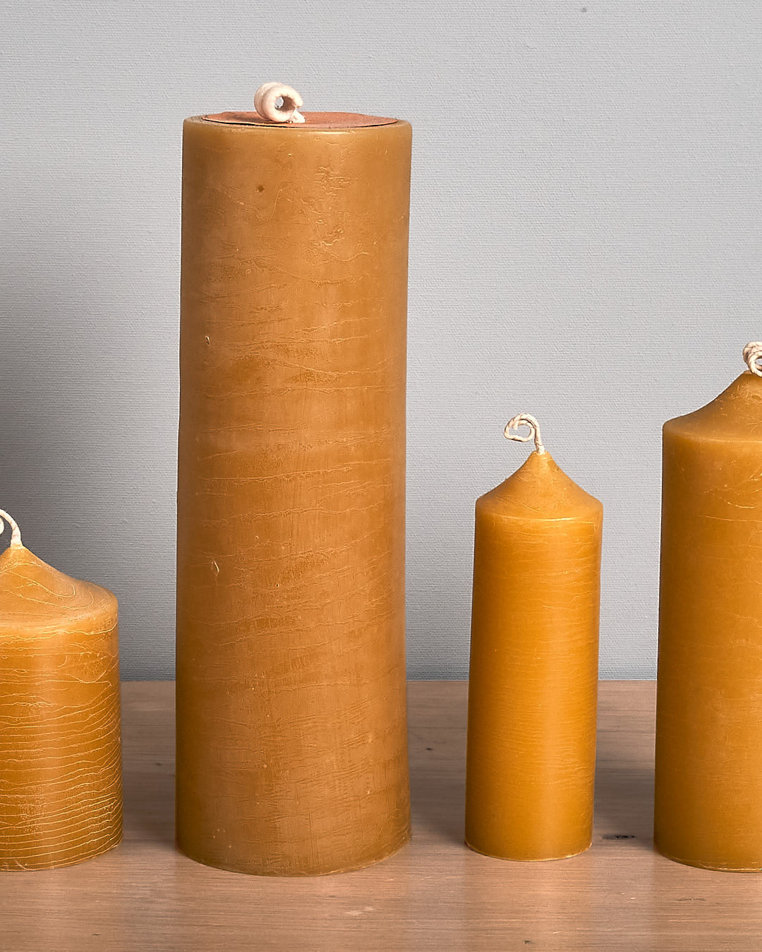 The Pillar Beeswax Candle – Extra Large by Hohepa Candles, with its tall and cylindrical shape, is displayed on a wooden surface against a plain gray background, highlighting its warm beige hue.