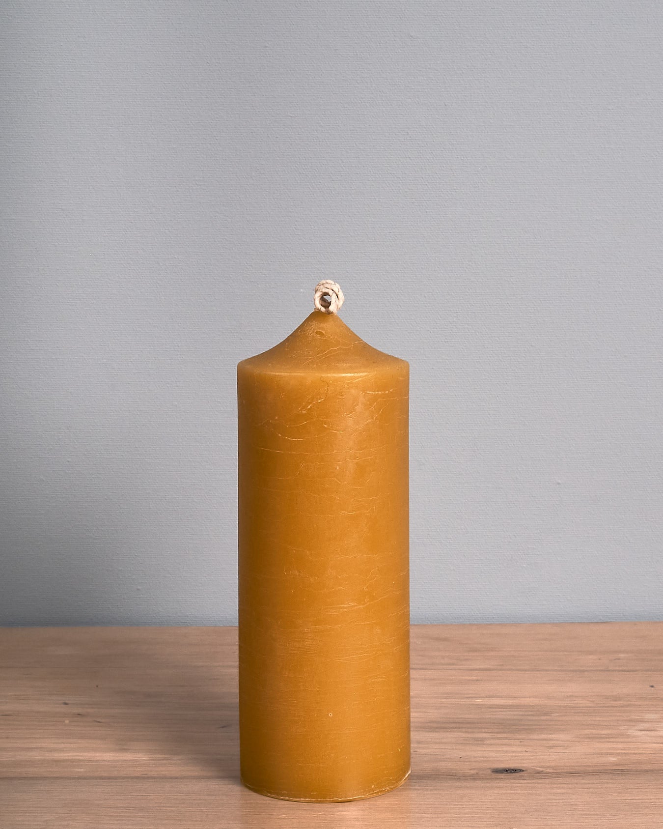 A tall Pillar Beeswax Candle from Hohepa Candles stands handcrafted in yellow on a wooden surface against a gray background, showcasing its natural beauty.