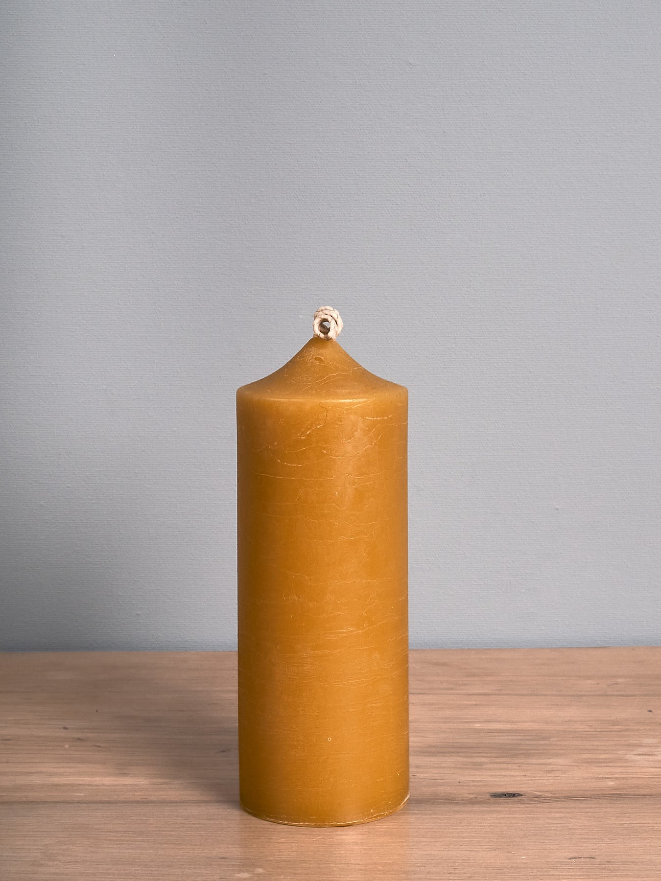 A tall Pillar Beeswax Candle from Hohepa Candles stands handcrafted in yellow on a wooden surface against a gray background, showcasing its natural beauty.